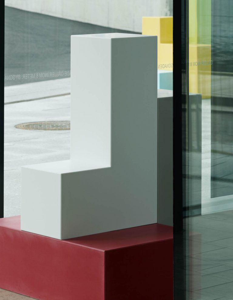 Skulptur inomhus bestående av ett rött rätblock i basen och två L-formade block i vitt och grått placerade ovanpå. Jacob Dahlgren, Tetris, 2012.