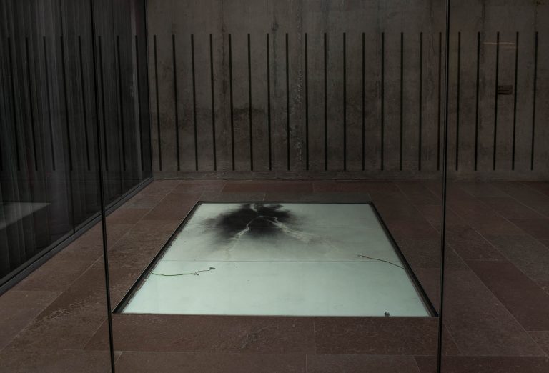 Den vita golvplattan med kol och två elsladdar. Nina Canell, Impulse Slight (100 000 Volt)