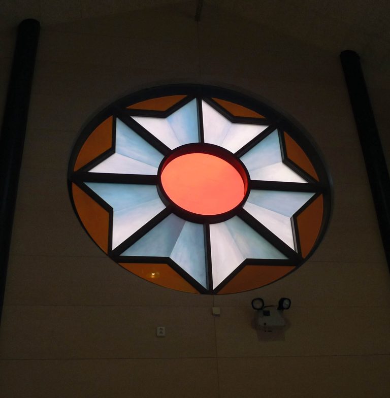 Ett cirkulärt fönster, tre meter i diameter, med digitaltryckt, laminerat glas. Motivet är en kokard, prisrosett. Cecilia Aaro och Matilda Fahlsten, Kokard, 2014.