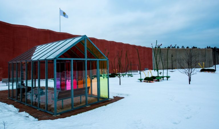 Litet växthus med olikfärgade glasväggar och snö på marken runtomkring. Thomas Nordström, Glänta, 2014.