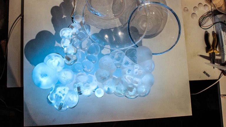 Bubblor av glas i olika storlekar som ger ifrån sig ett turkost sken. Fredrika Linder, W