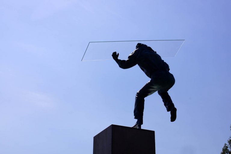 Skulpturens armar är höjda, på handflatorna balanserar han en glasskiva. Heinrich Müllner, Flyer, 2014