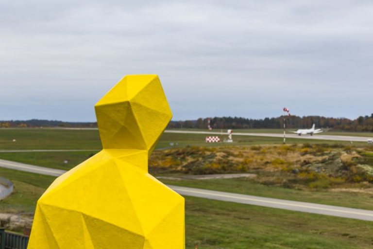 Gul skulptur av en man som blickar ut över ett flygfält, detalj. Xavier Veilhan, Julian.