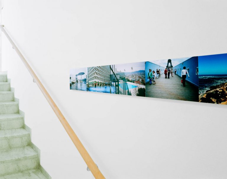 Del av sammanhängande fotoserie i trapphus. På en bild skymtar Eiffeltornet, på en annan en inhägnad badbassäng och ett mycket högt hus. Franz Ackermann, Travelling North, (2007).
