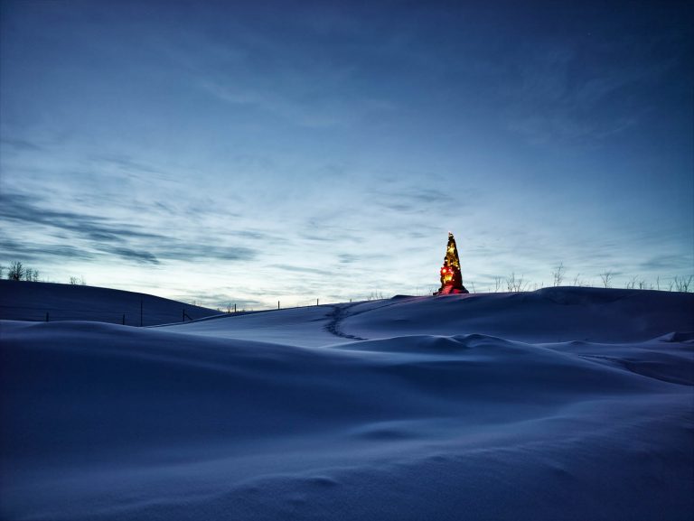 Natthimmel. Snölandskap. På avstånd lyser och glittrar Totem på sin kulle. Oskar Aglert, Totem.
