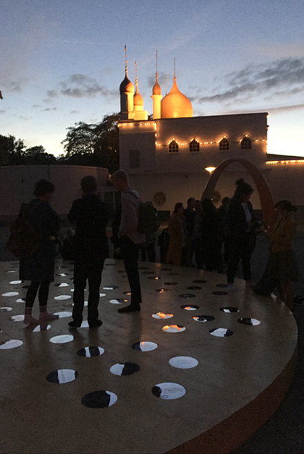 Flera personer på ett runt trägolv med små cirkulära speglar. Nisrine Boukhari, Imaginary Wholeness/Fragmentary Reality.