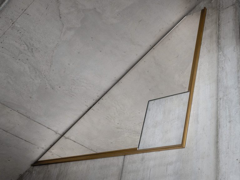Hängd spegel med fyrkantigt hål i mot betongvägg