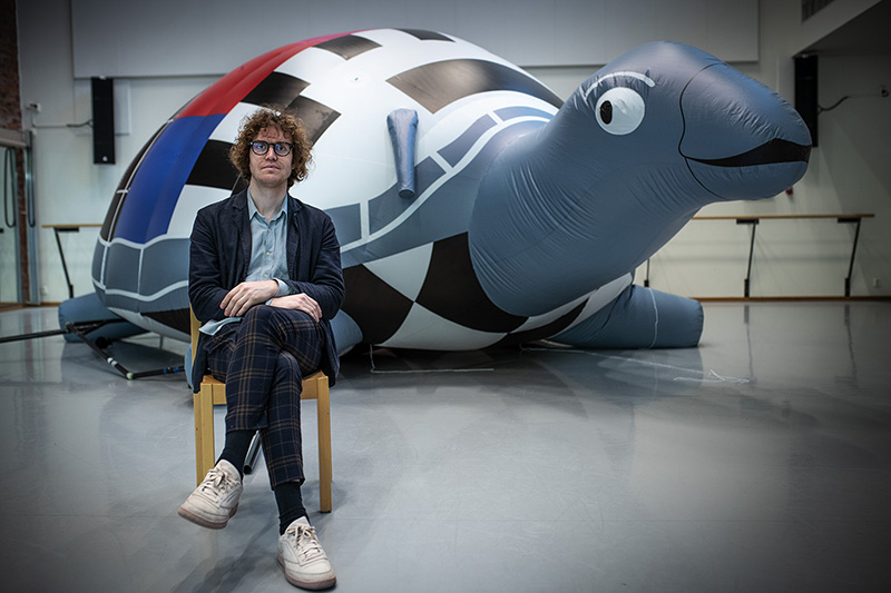 man sitter på en stol framför en uppblåsbar sköldpadda.