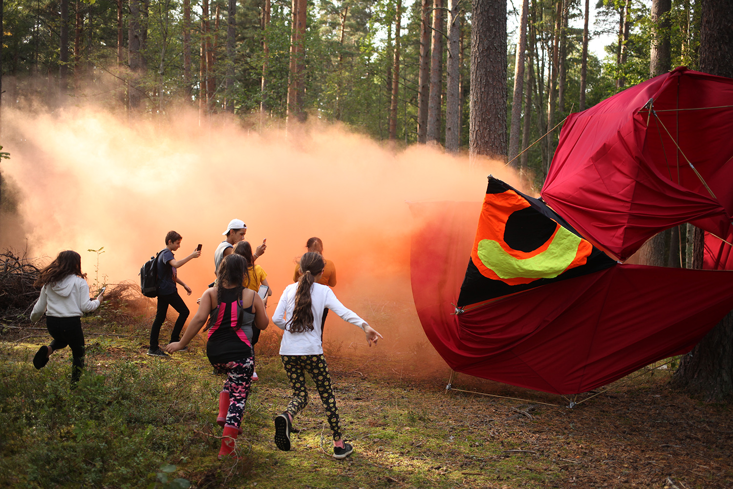 springande barn i en skogsdunge. en stor rödboll rullar ner och röd rök hänger i luften.