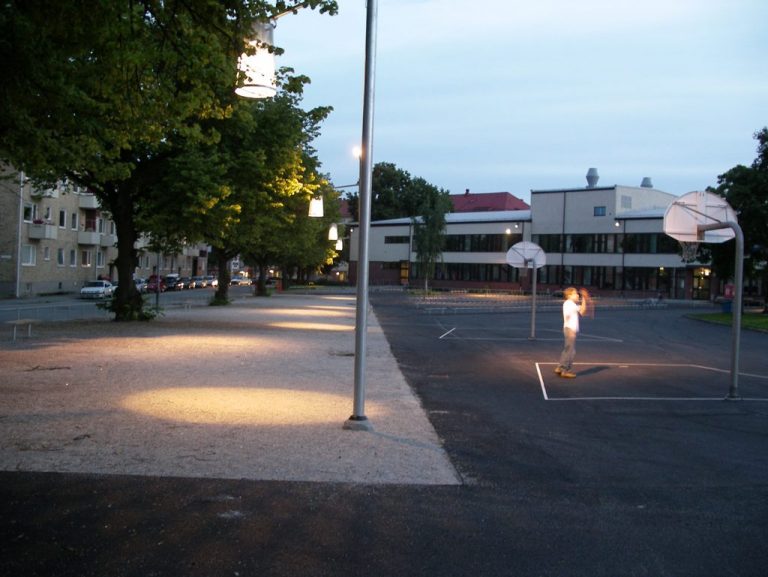 Lampor lyser upp en skolgård där en ensam person spelar basket.