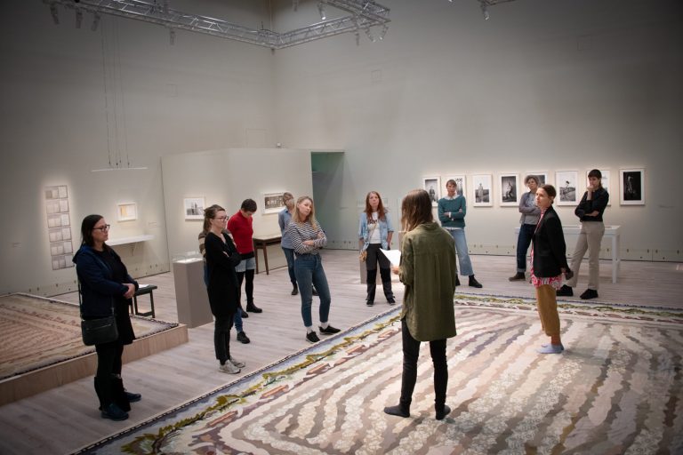 Personer står och lyssnar på en person som pratar