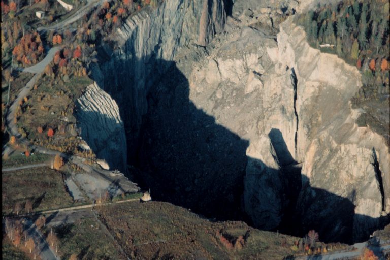 Ett djupt gruvschakt sett från luften med hus vid sidan av kanten.