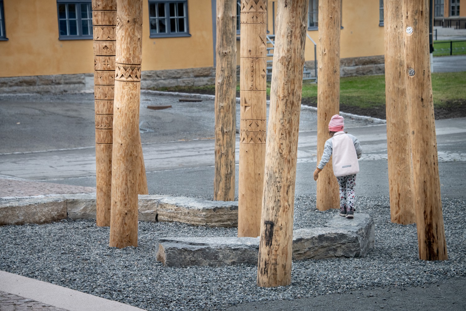 Barn går på avlång sten bland träpelare med olika mönster