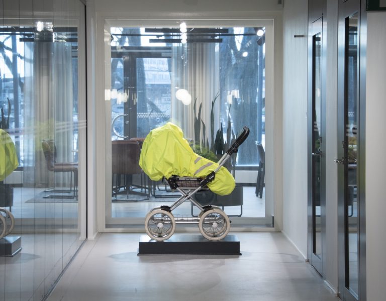 En gul barnvagn i en korridor med glasväggar.
