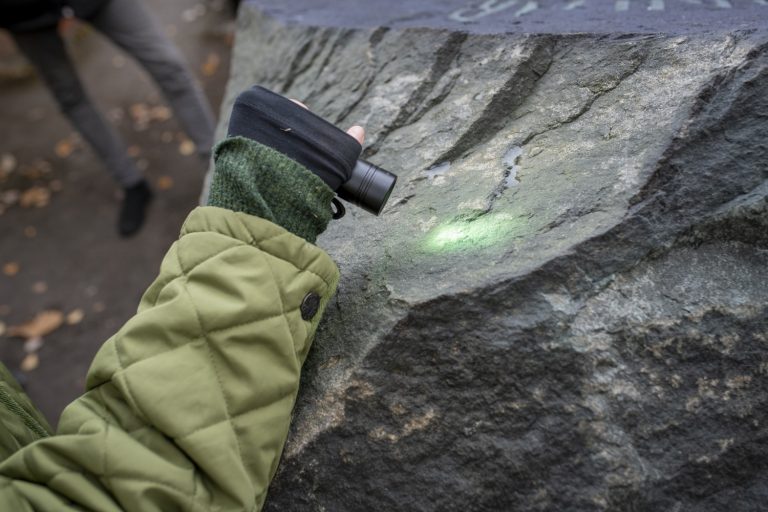 En person lyser på en sten med ficklampa. Stenen är fluorescerande.