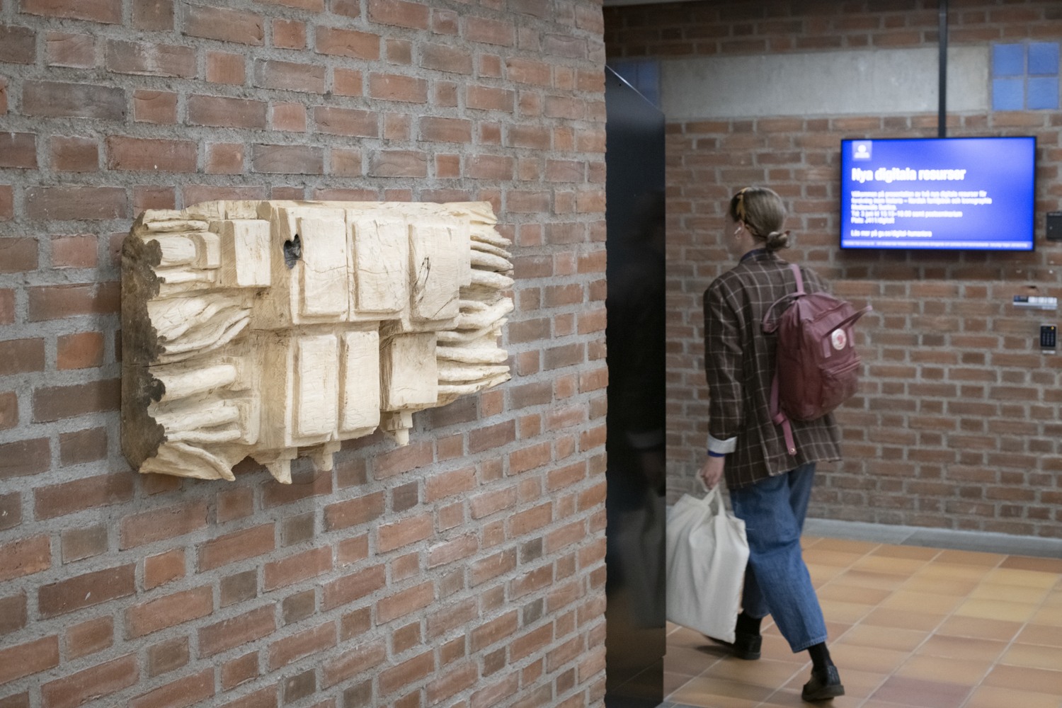 En kvinna som går förbi en tegelvägg med en skylt på