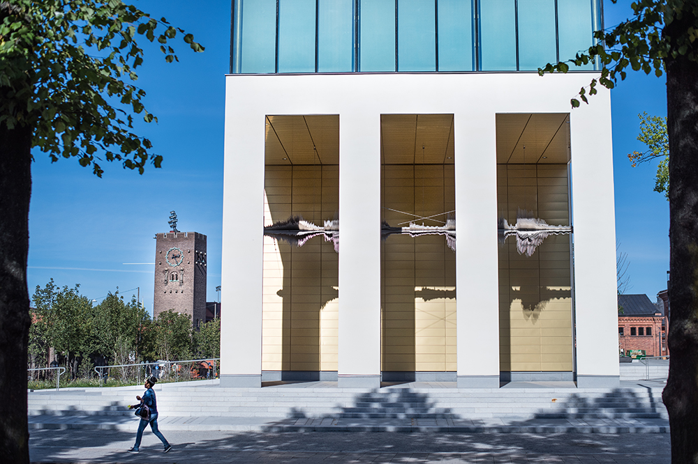 Man går förbi byggnad med vita pelare och en guldloggia där en skulptur hänger i loggian