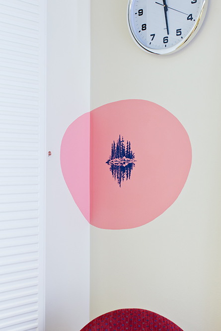 Skär rundel på väggen med en blå teckning av tallar som speglar sig i ett vatten. Gerd Aurell, Till mitten hunnen.