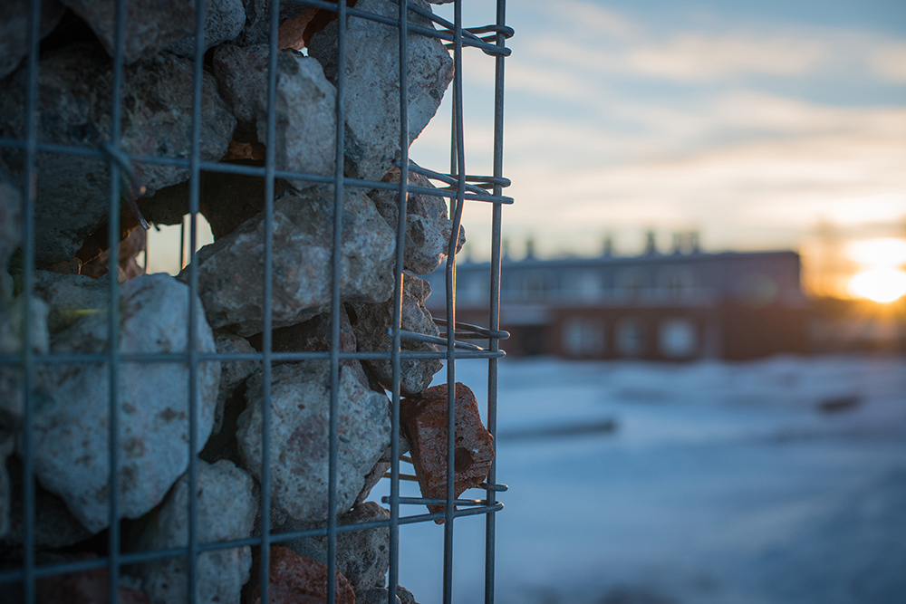 Detalj, gabion fylld med rivningsmassor. I bakgrunden ett hus. Sofia Sundberg, Karl Tuikkanen, Ingo Vetter, Gruvstadsparken.