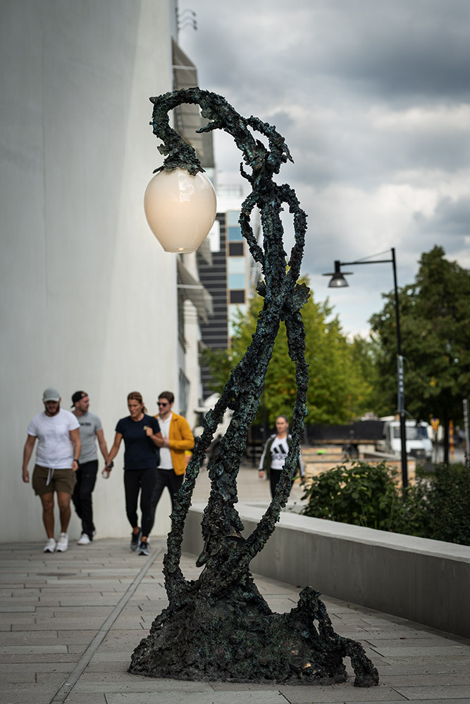 Stående helhetsbild på Lyktan med människor gående mot konstverket.