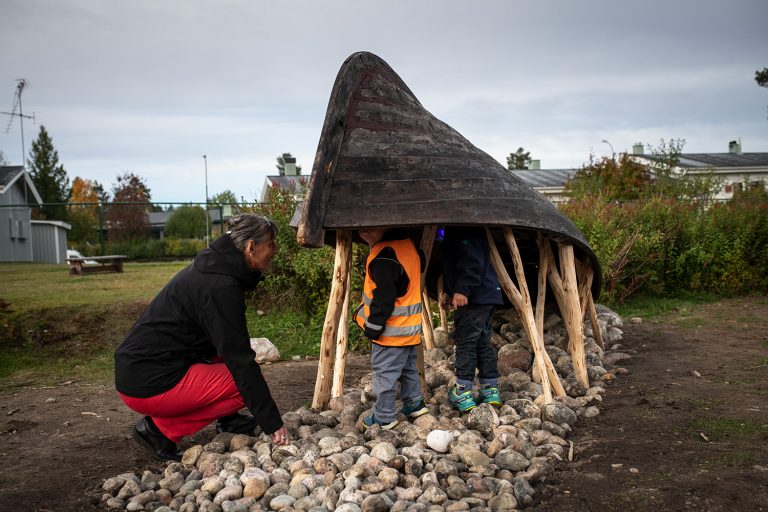 Barn som står under en båt och leker.
