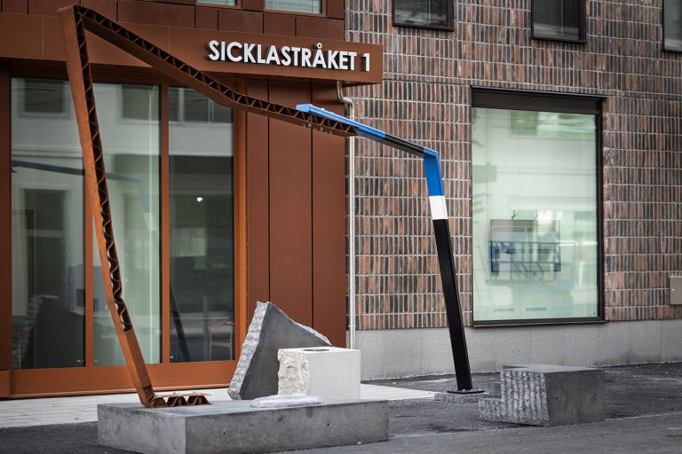 Konstverk av metall och sten utanför hus.