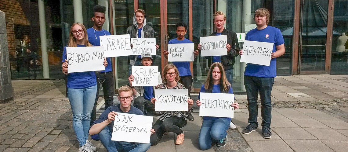 En grupp människor håller plakat med yrkestitlar i händerna.
