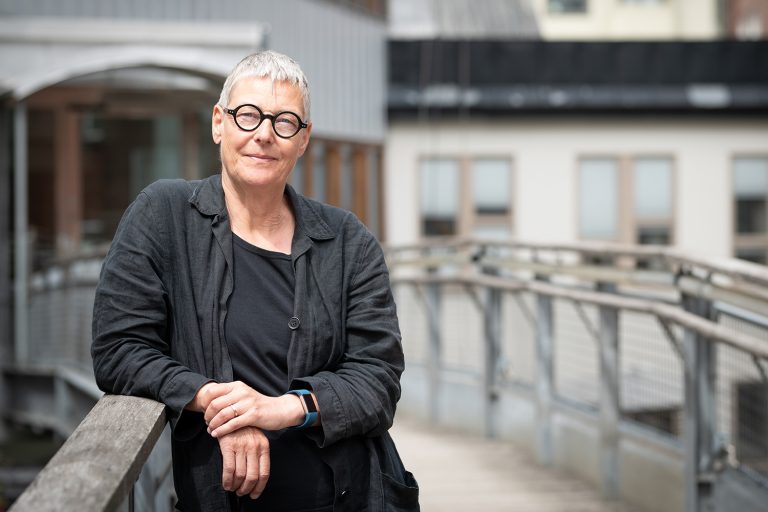 Kvinna med kort hår och glasögon står lutad mot ett räcke.