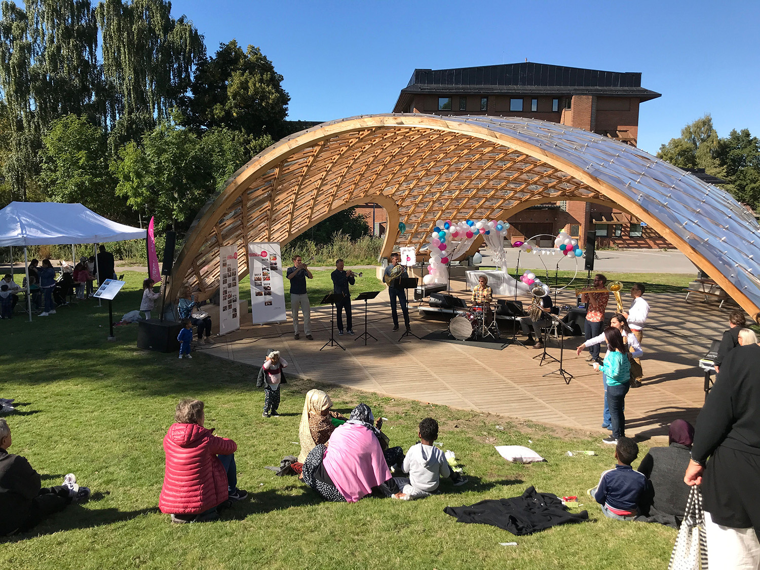 Människor sitter under en trä paviljong