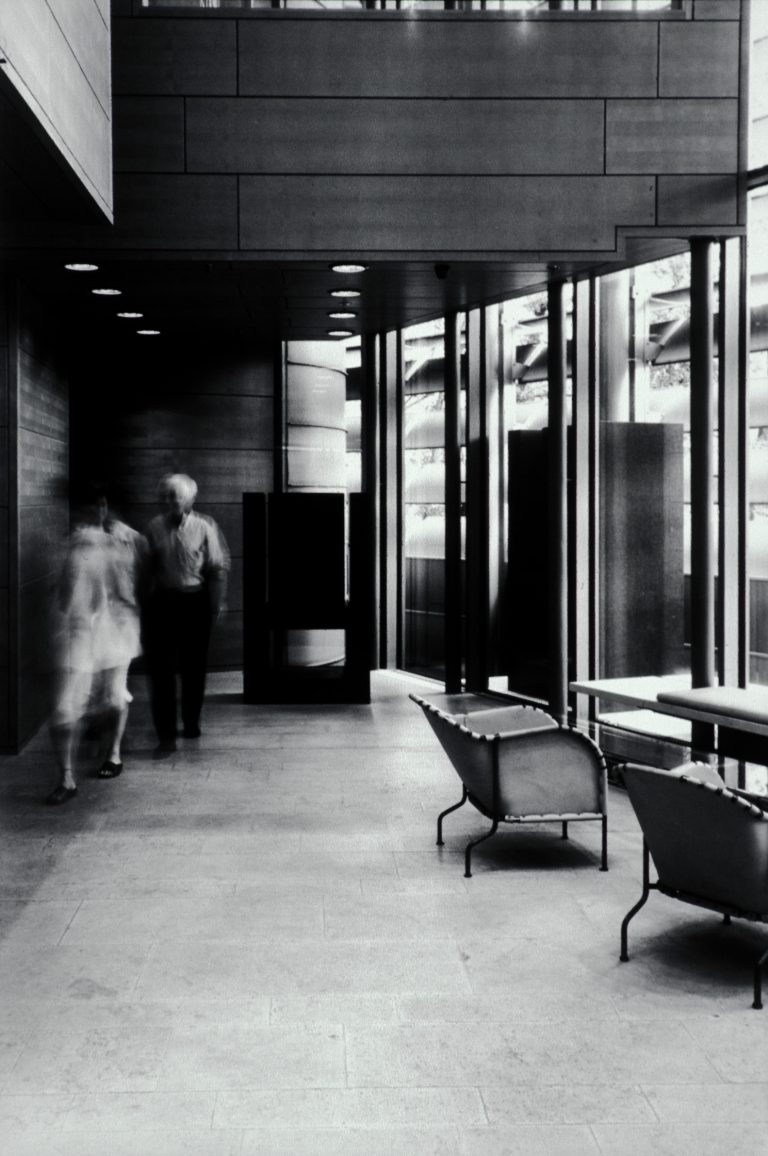 Interiörbild från långsmalt rum med en glasvägg, stolar och en skulptur