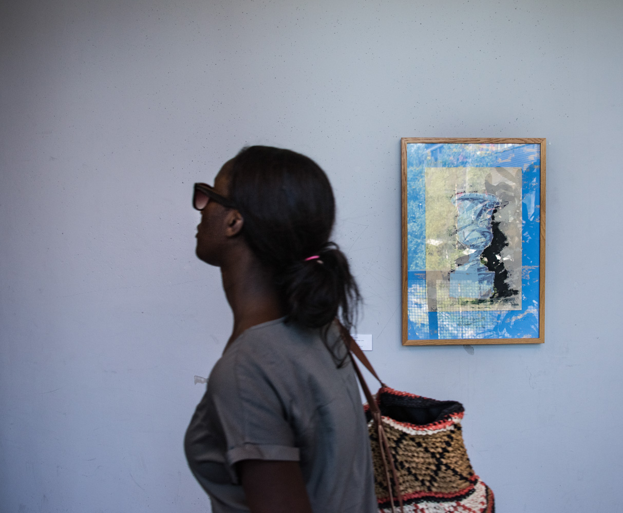 Kvinna går förbi en målning som hänger på en vit vägg