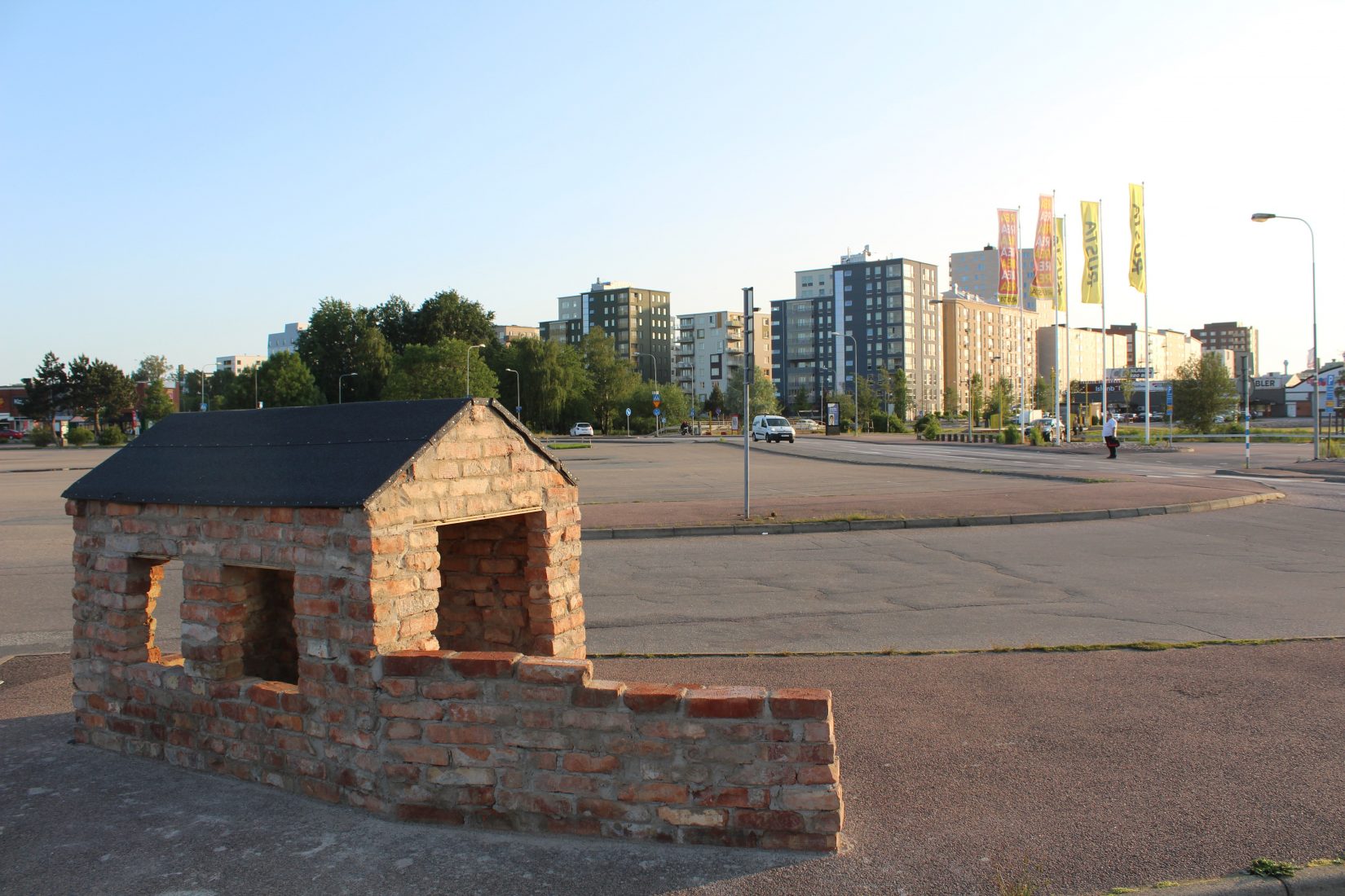 Litet hus av tegel på stor parkeringsplats