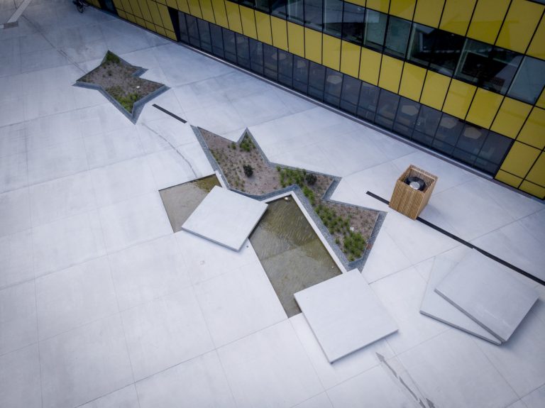 Närbild på torg där några några betongplattor lyfts upp och vatten finns under.