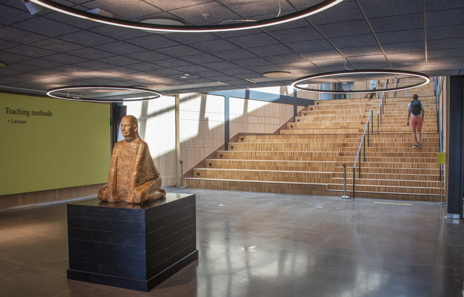 I en entré, framför en bred trappa, finns en träskulptur som består av en sittande man.