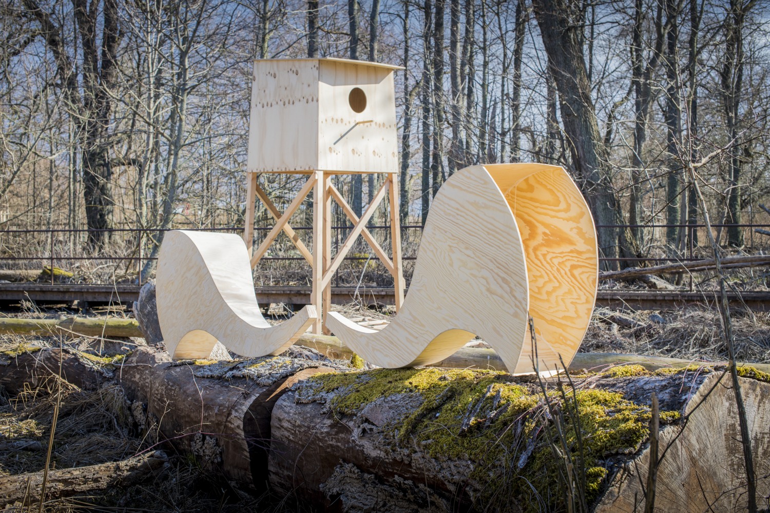 En stor fågelholk uppsatt på reglar och två stora lurar av plywood liggandes på marken.