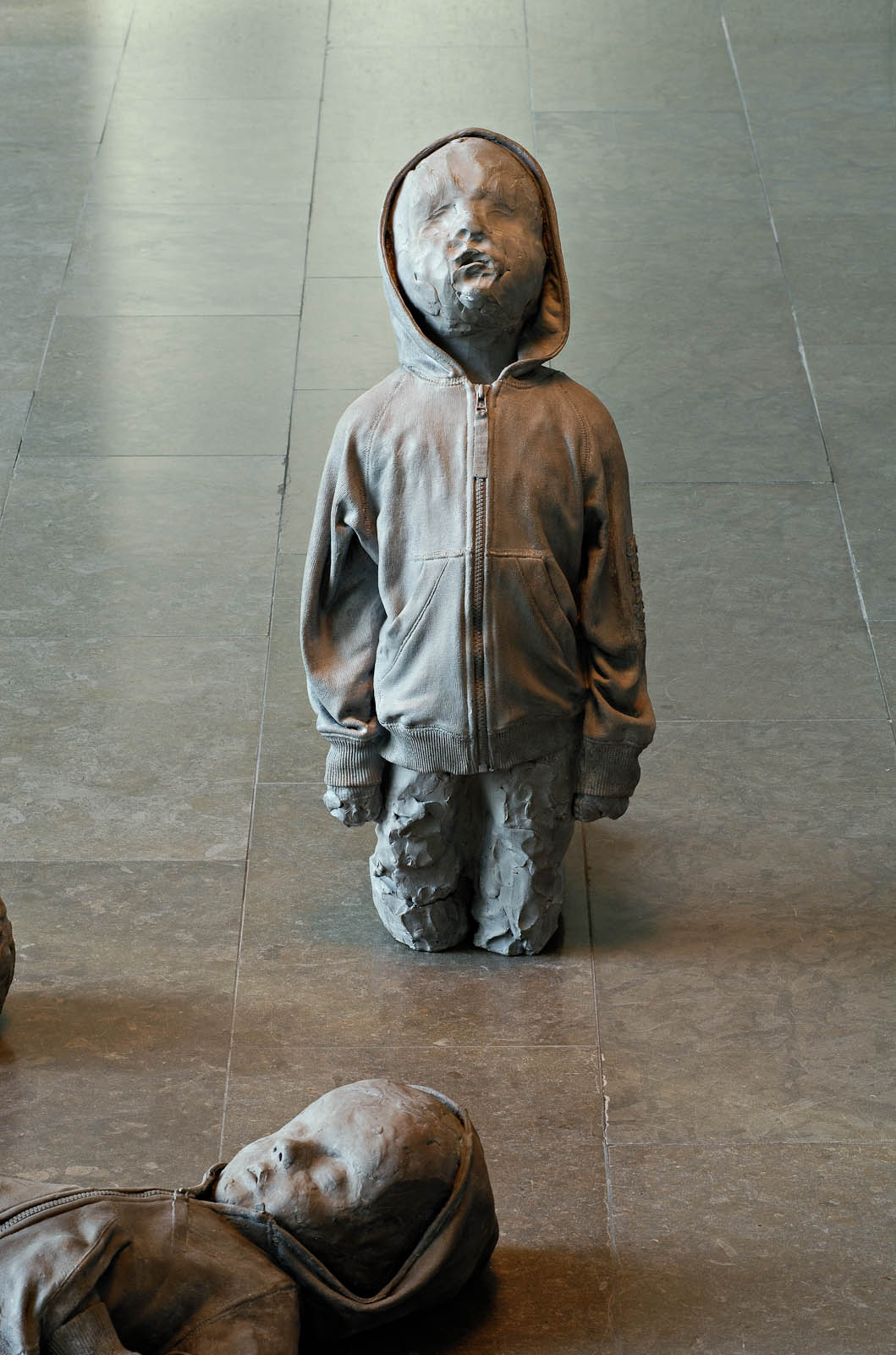 A child wearing a hood, on is knees looking upwards.