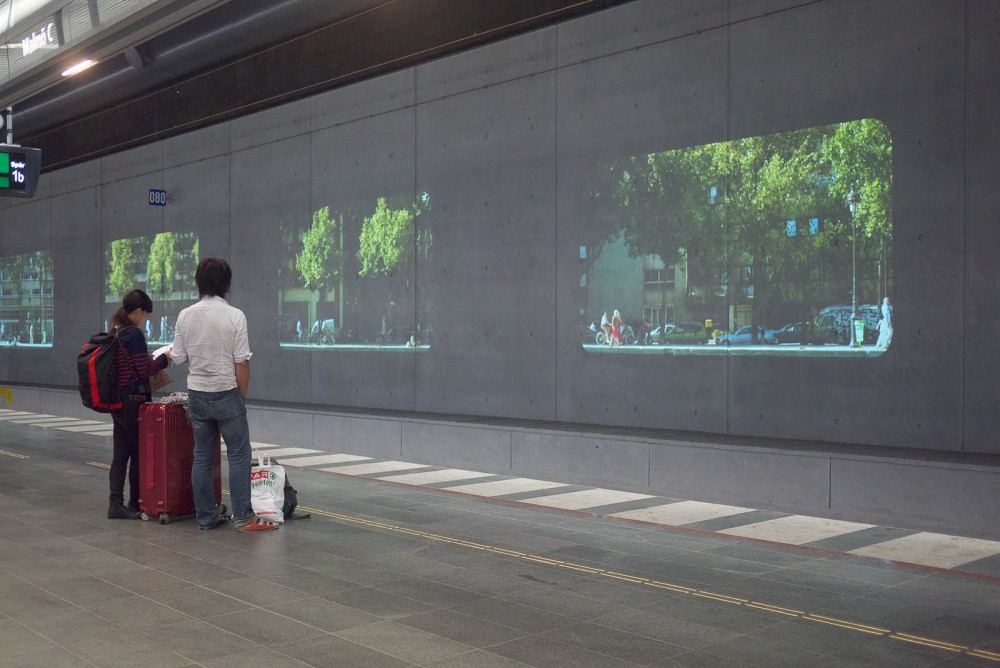 Two people with luggage looking at projections while waiting for the train.
