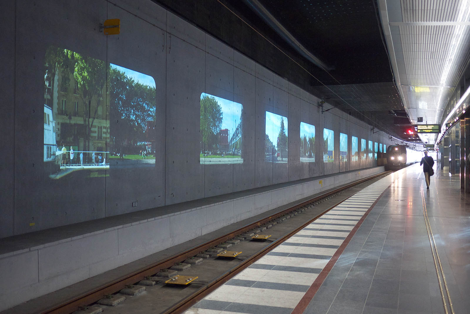 A train entering the station. On the wall projections of houses and trees.