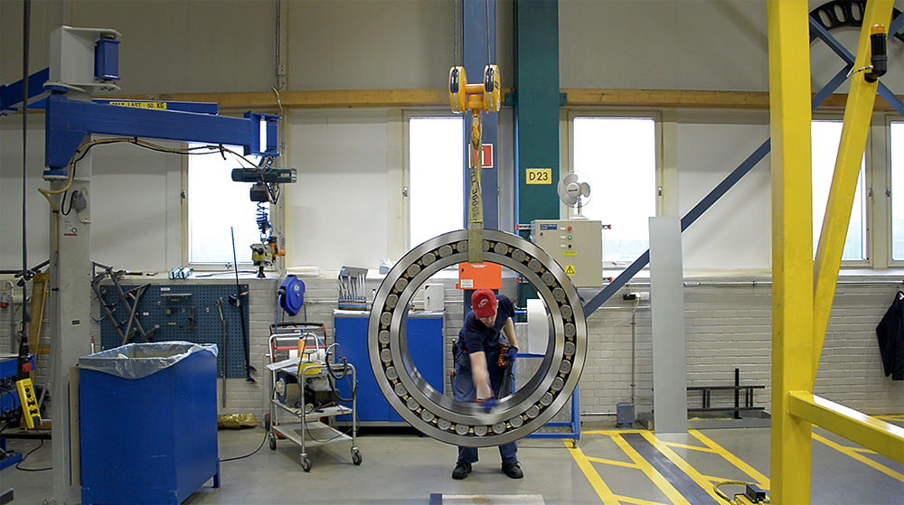 En man rengör ett stort stålhjul som hänger i en takkran i en industrilokal.