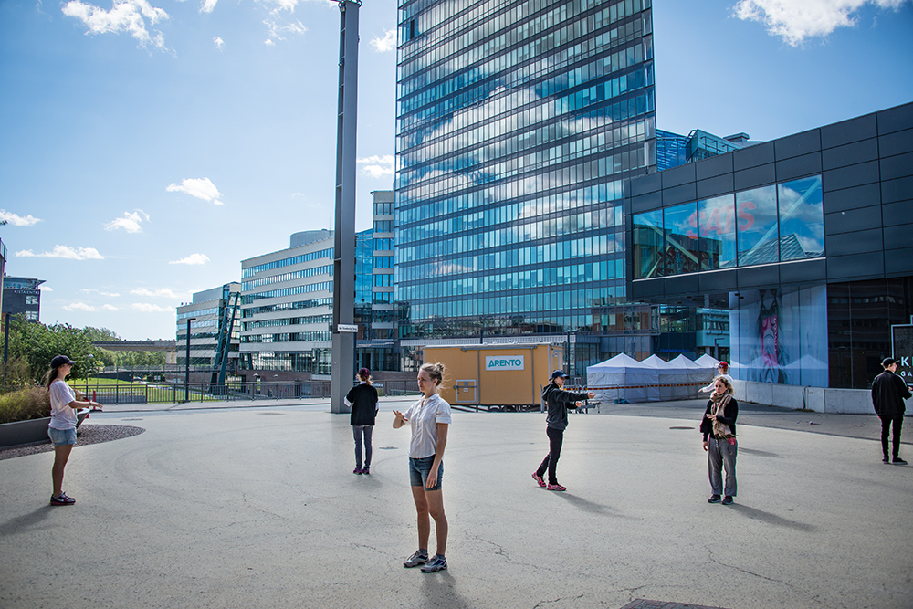 A group of peopela standing outside , each looking in their own direction. In the background a high-rise building.