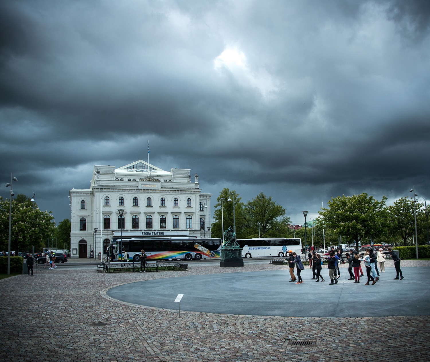Clouds over Stora Teatern in Malmö. In the corner av the picture a group of people are making movements with their arms.