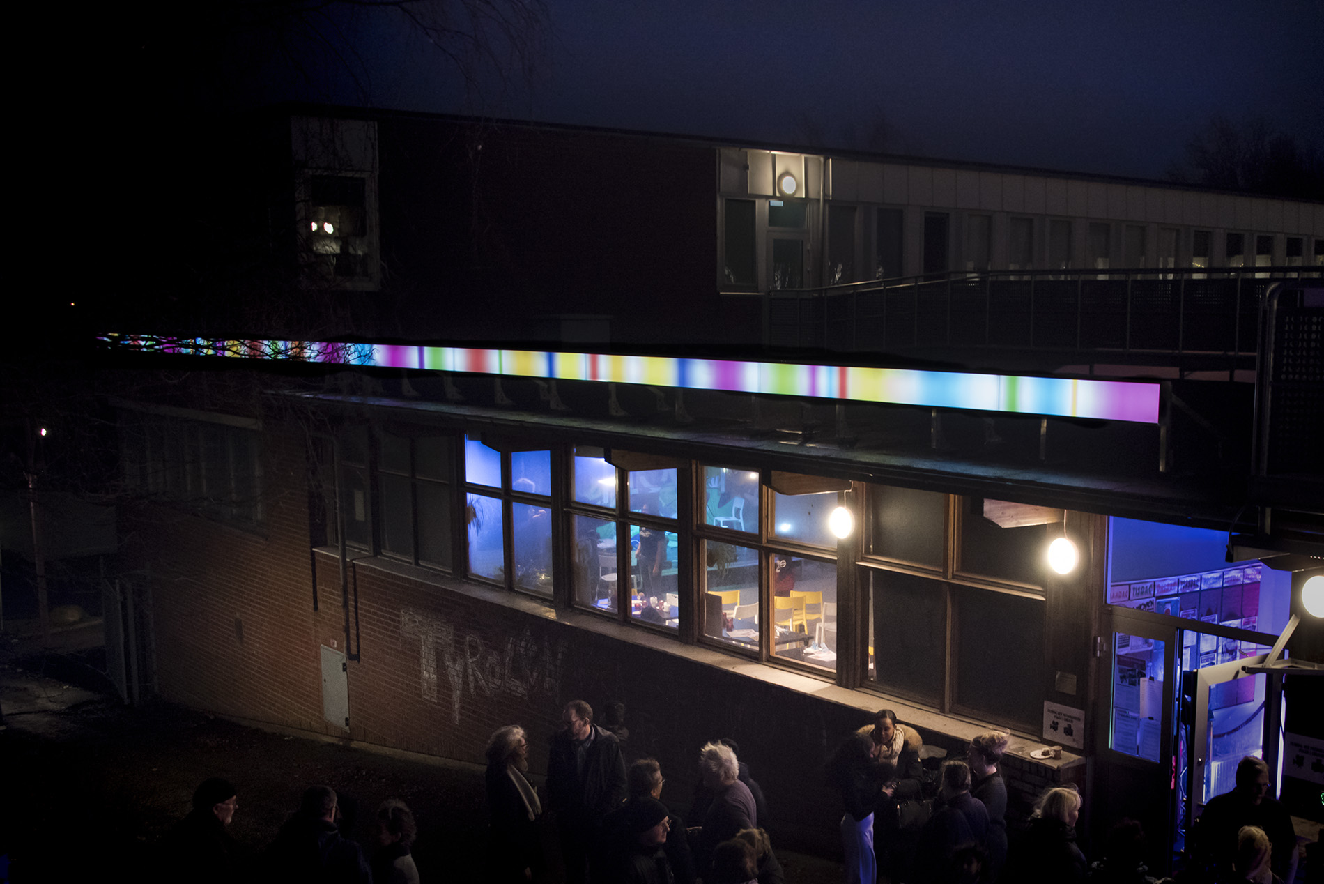 A series of light boxes running across the facade of a brick wall. Shot at night, when the artwork is light.