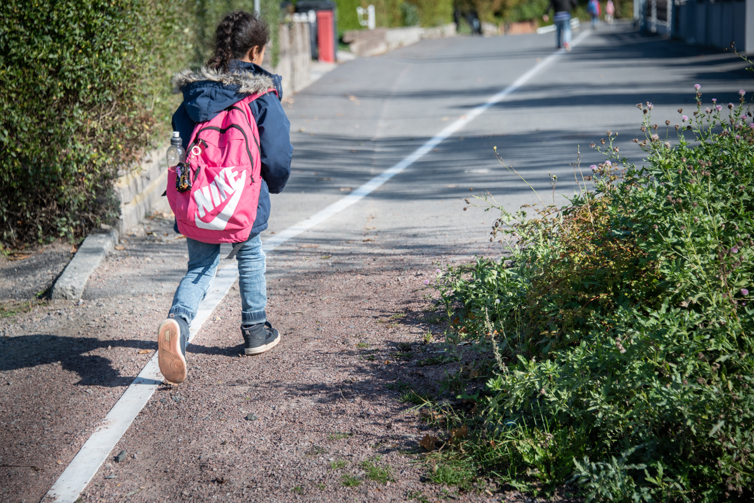 A girl with a backpack walks along a white line.