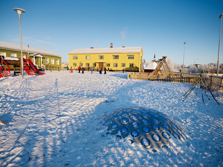 En grön och en gul skolbyggnad i skarp vintersol. På lekplatsen faller skuggorna långa över termonoden. Markus Lantto, Termonoder, 2009