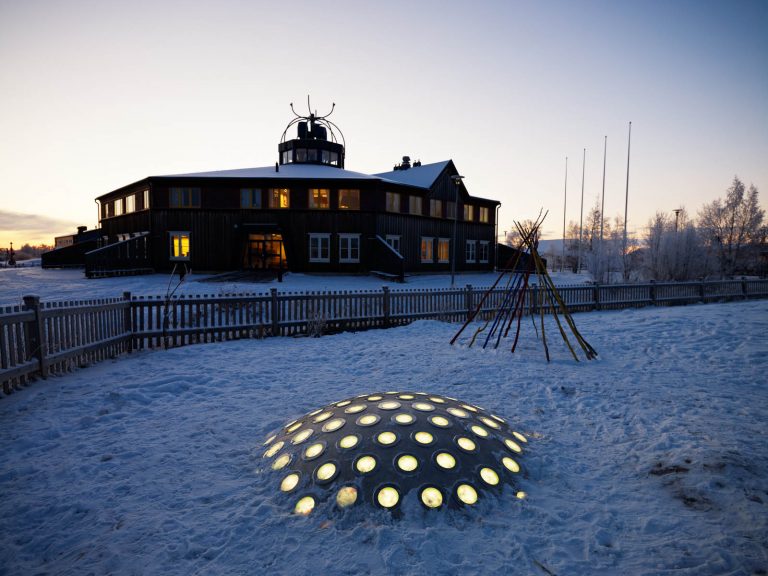 Termonodens lampor lyser gula på den mörka skolgården. I bakgrunden en upplyst byggnad. Markus Lantto, Termonoder, 2009