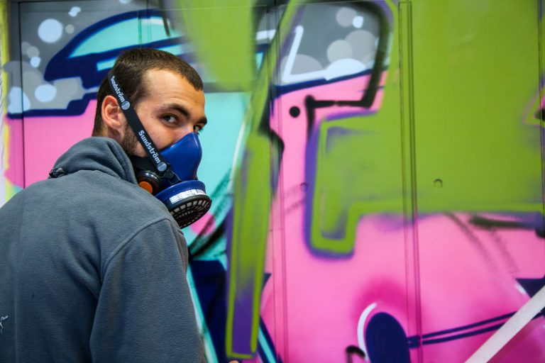 En man med gasmask framför en graffitimålning. Pärra Andreasson, Vad Vi Vill
