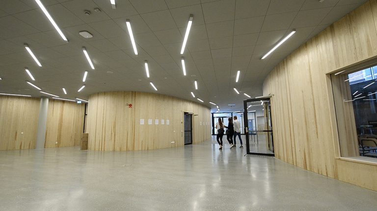 Några studenter går genom en korridor med träpanel och lysrör i taket. Jonas Dahlberg An imagined city