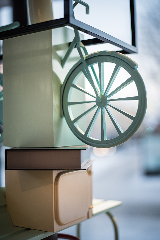 Detalj. I pelaren ingår en liten grön cykel ovanpå en liten bok. Sirous Namazi, Rekonstruktion