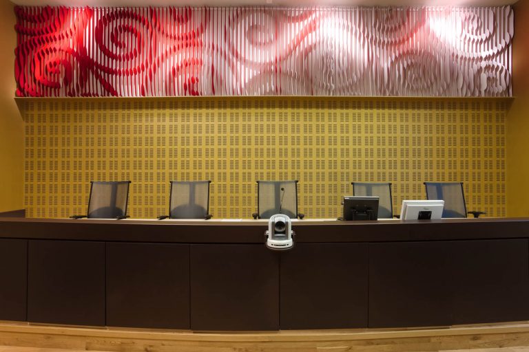 Panel på väggen ovanför domarbordet. Röd-vitt med utskurna spiralliknande mönster. May Bente Aronsen, Lyssnande vägg