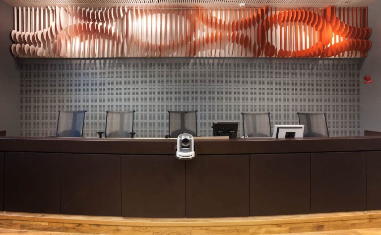 Panel på väggen ovanför domarbordet. Orange-vitt med utskurna cirkel- och vågmönster. May Bente Aronsen, Lyssnande vägg